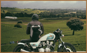 A man standing over a motorbike looking at the countryside