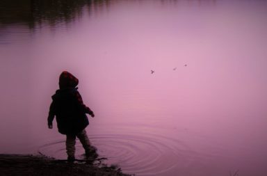 A boy standing in a pond making ripples with his foot