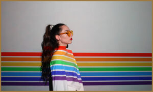 An autistic woman with the lgbt flag painted over her and the wall behind