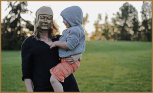 An autistic woman with a gold mask holding a child
